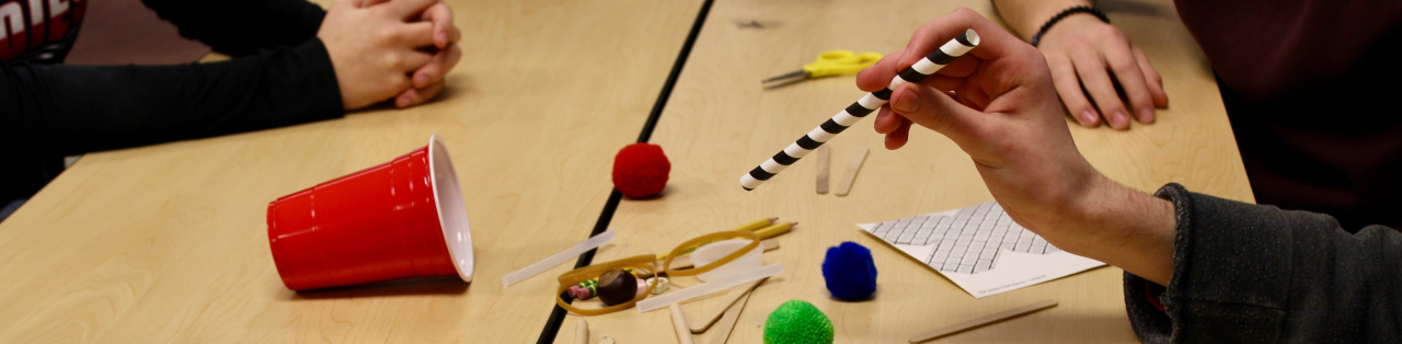 hands building a catapult with sticks, straws and rubber bands