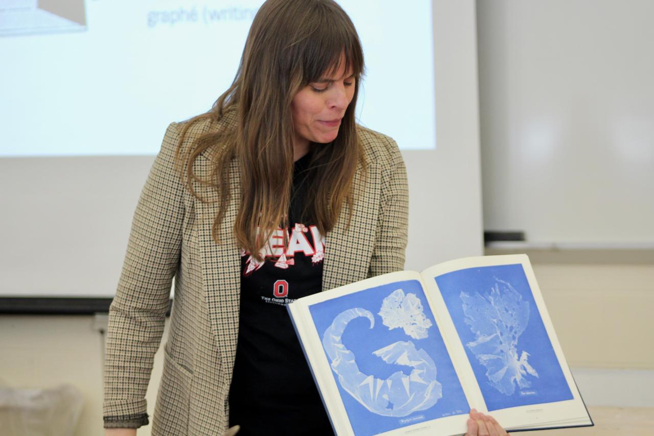 Kate Shannon holding a book and speaking to an unseen group