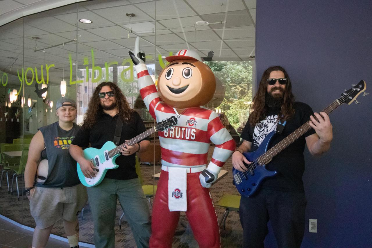 three members of a band posing with a statue of Brutus Buckeye