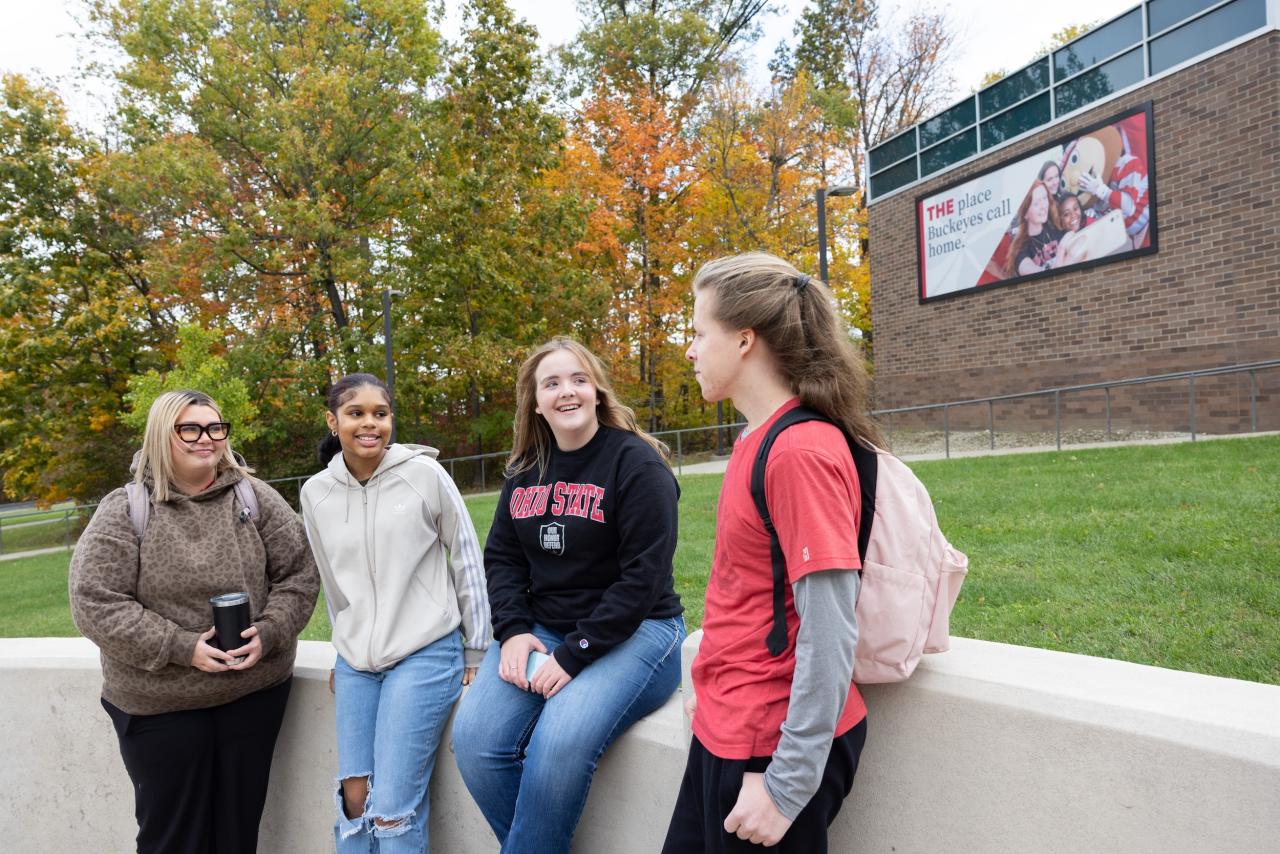four students sitting outside on a short concrete wall