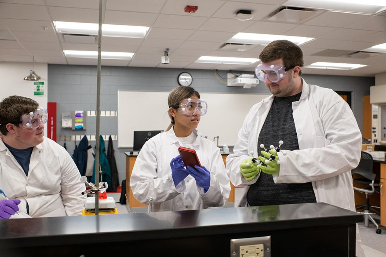 three students wearing white lab coats in a lab setting.