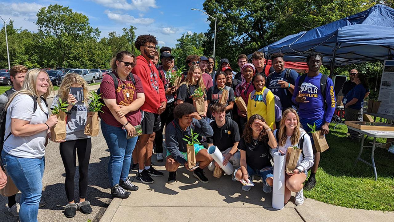 A large group of students hold native plants given out at a pollinator-focused campus outreach event.