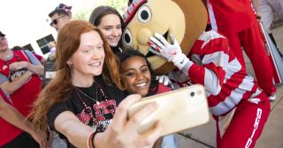 Three female students posing with Brutus Buckeye for a selfie picture