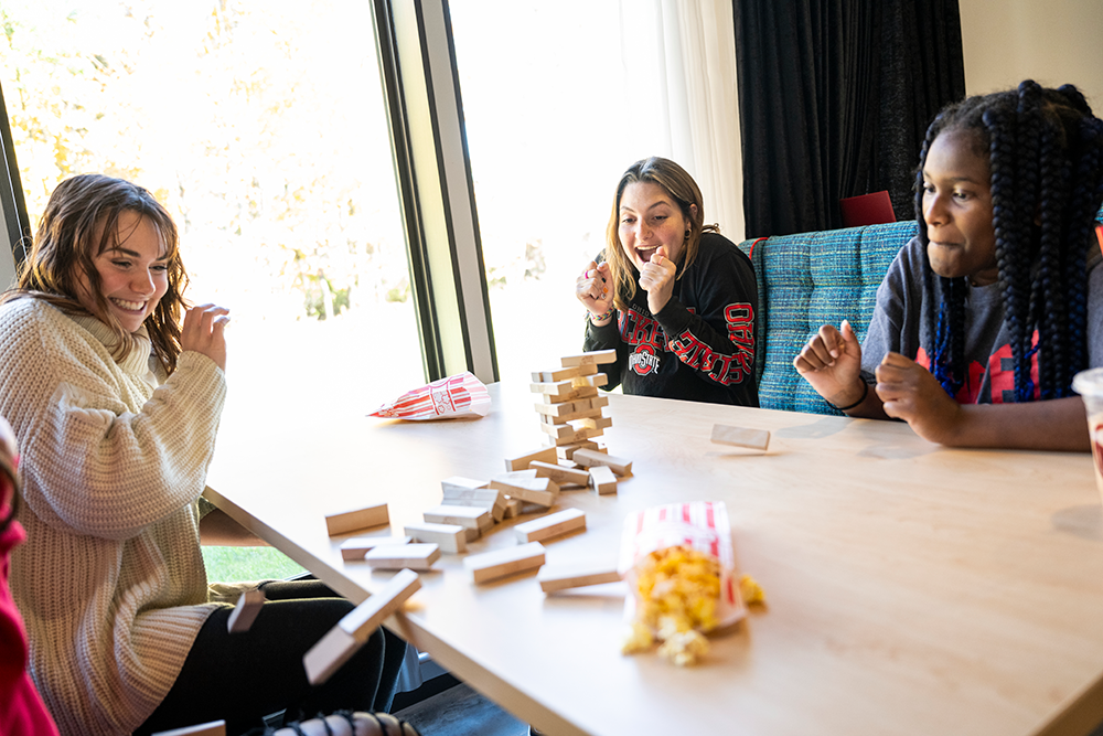 Three female students sitting at a table playing the blocks game Jenga