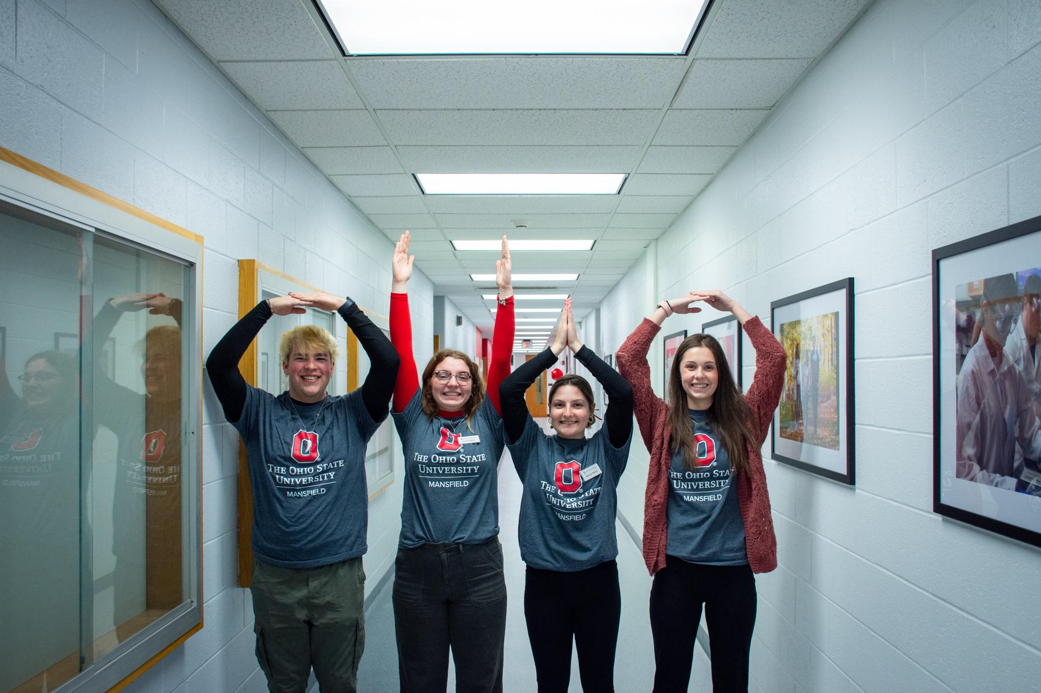 Four students in a hallway holding up their hands spelling out O H I O.