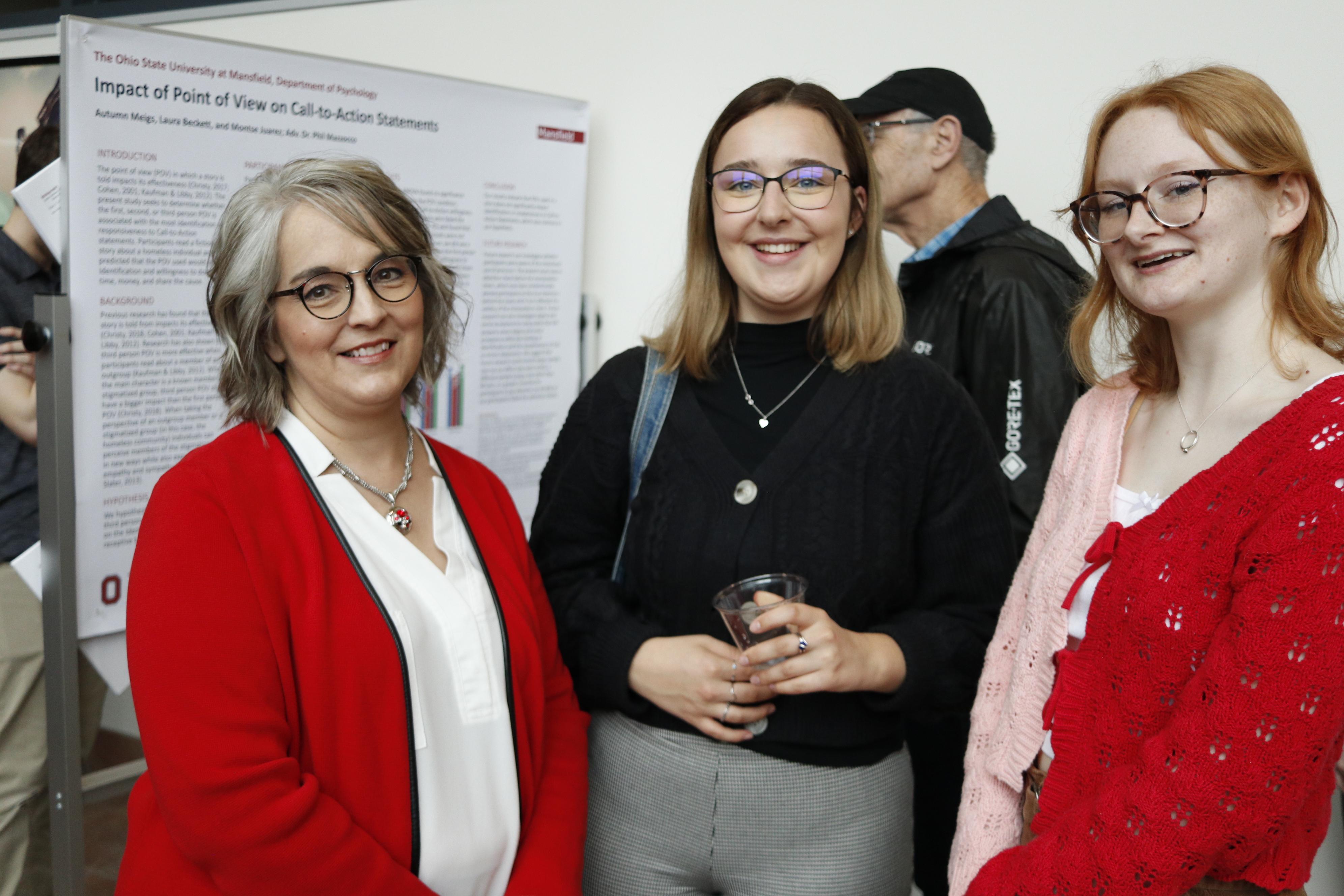 three women smiling posing for the picture in front of a research poster