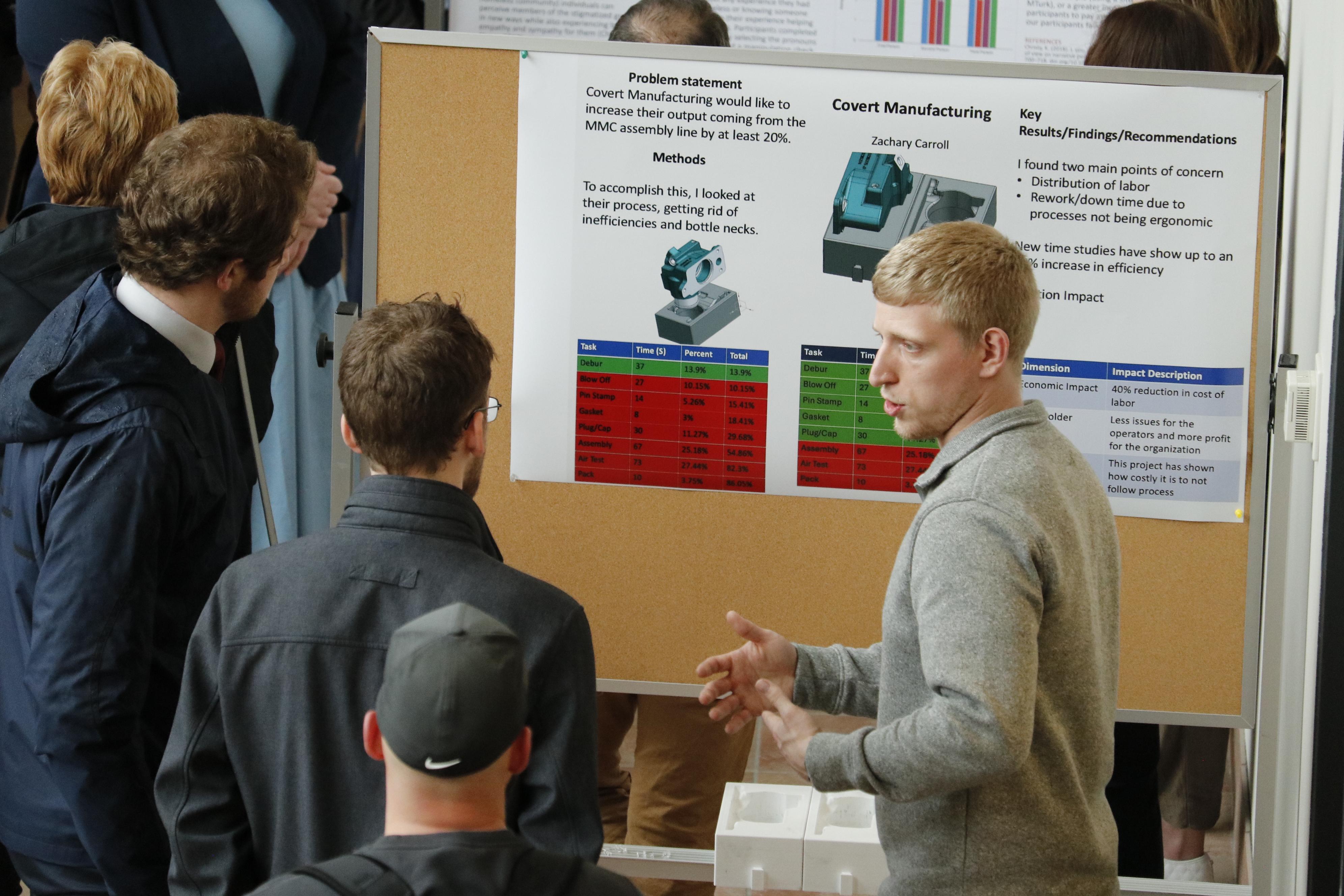 a male student explaining his research poster to two other males