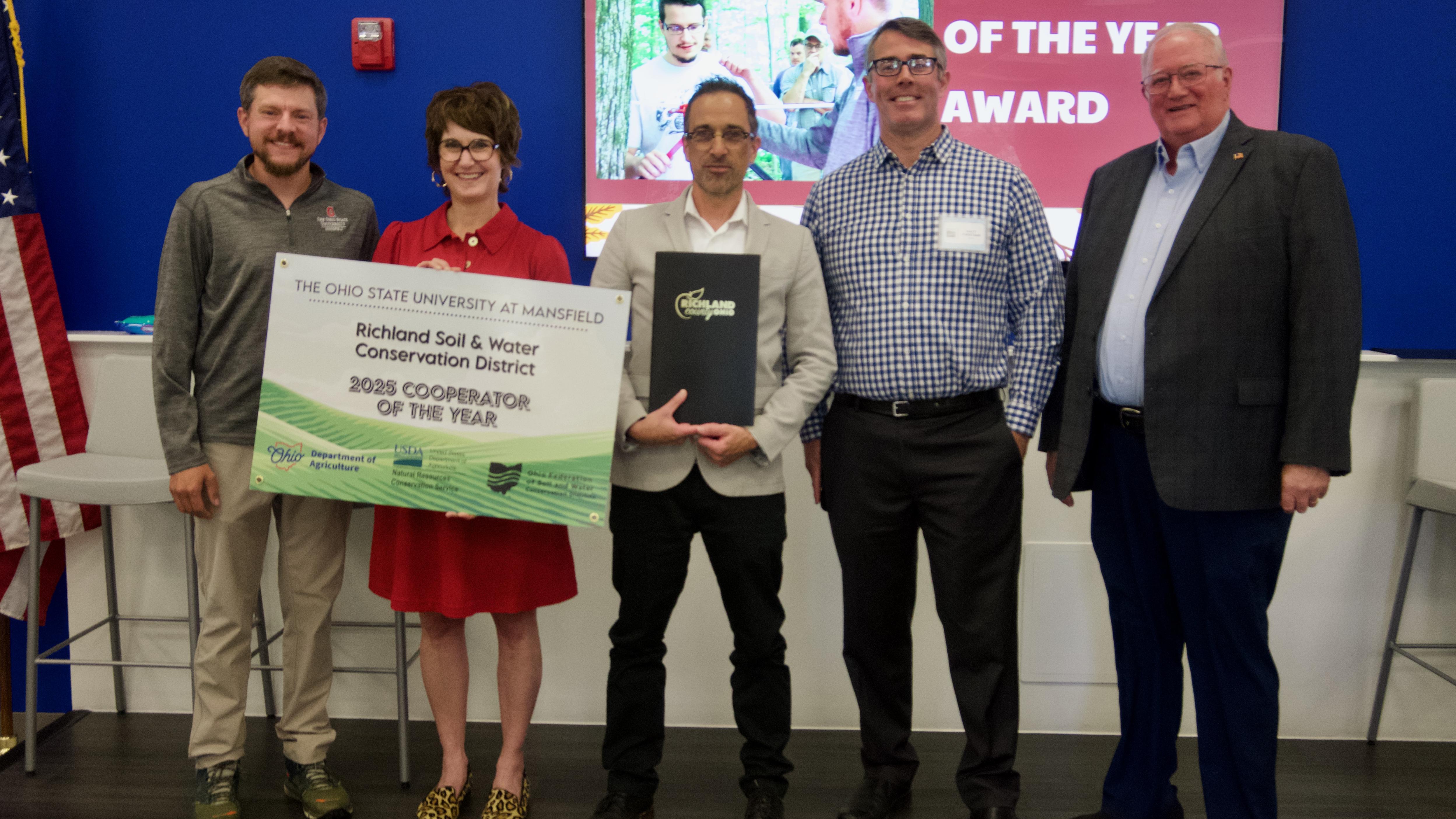 four males and a female posing with a banner stating 2025 cooperator of the year