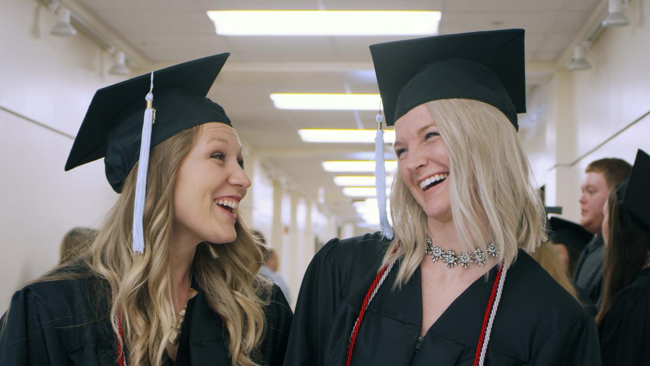 Two females wearing graduation attire laughing.