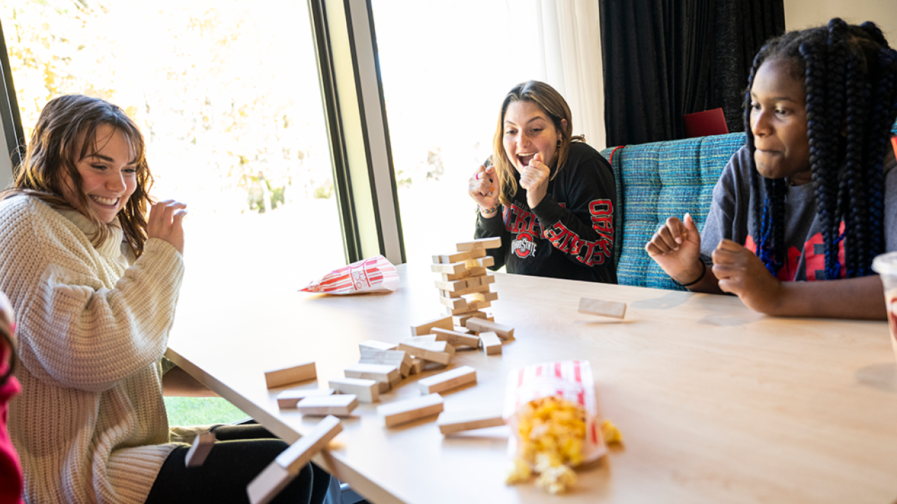 Three female students sitting at a table playing the blocks game Jenga