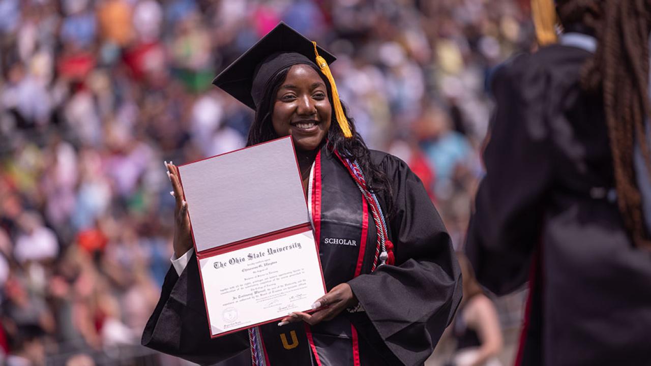 student at commencement holding a diploma and posing for the picture