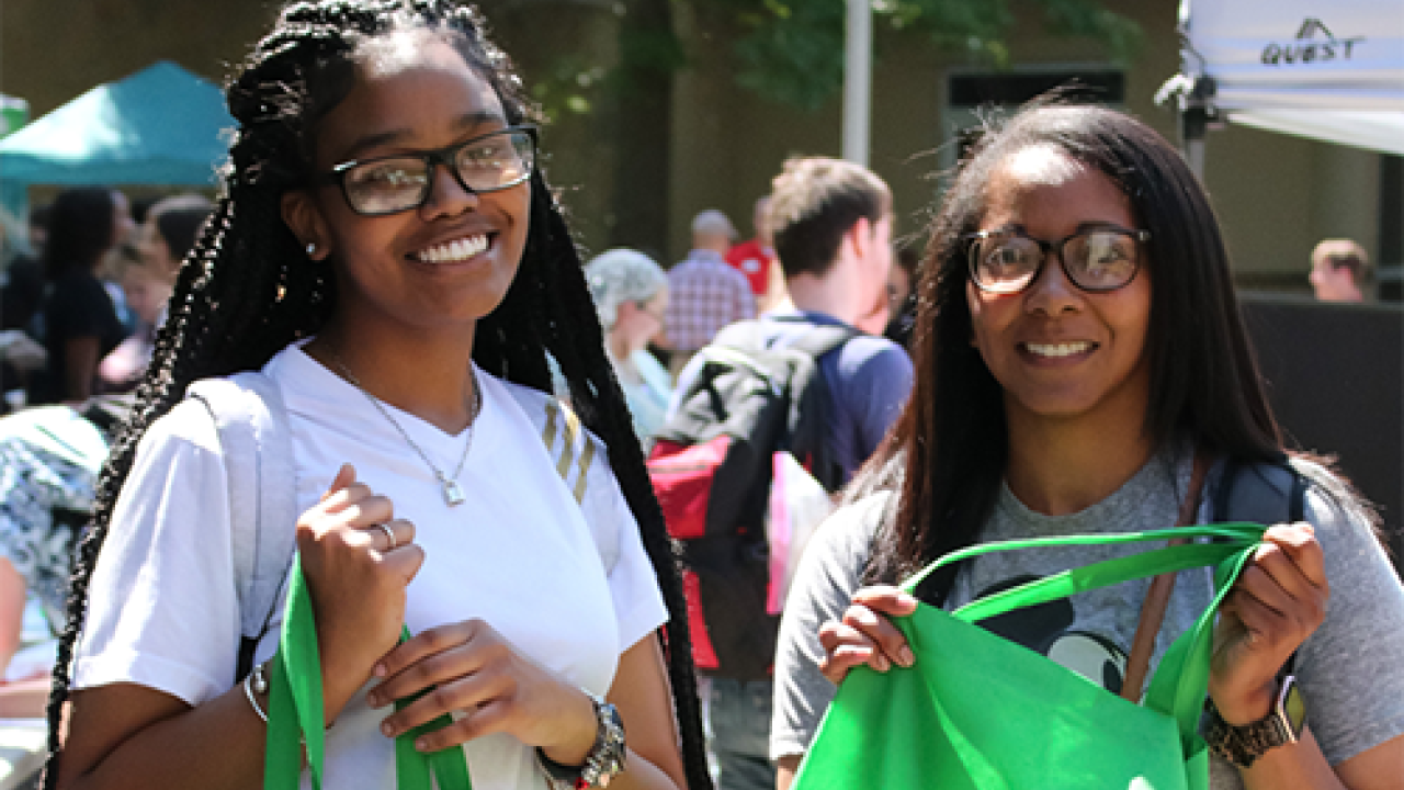 two students posing holding green bags