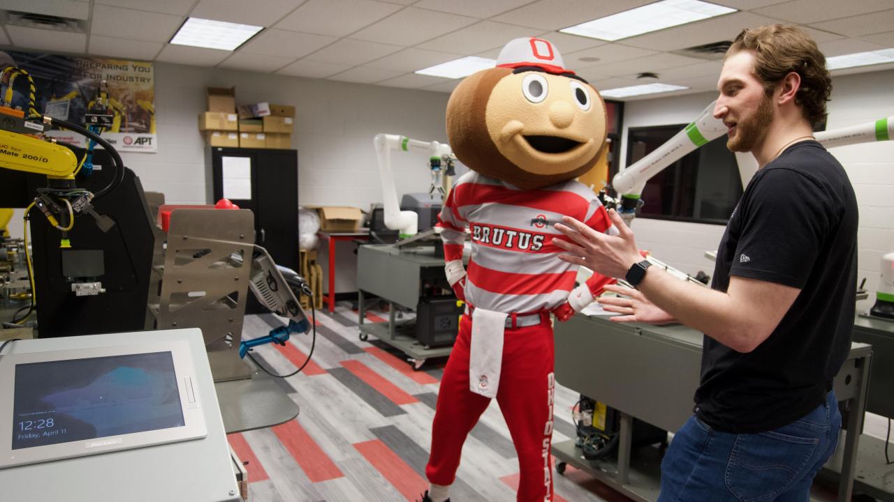 a male student and Brutus Buckeye standing in a robotics lab