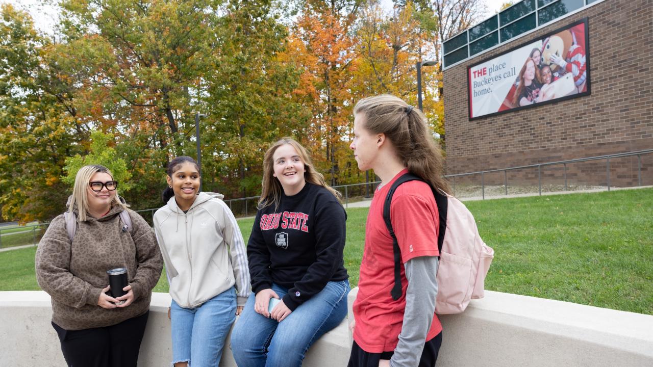 four students sitting outside on a short concrete wall