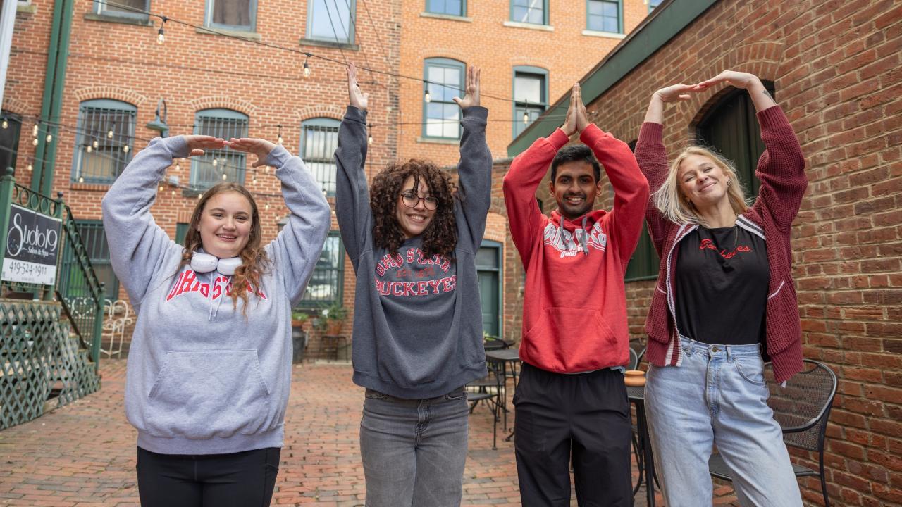 four students hold their arms up to spell out Ohio
