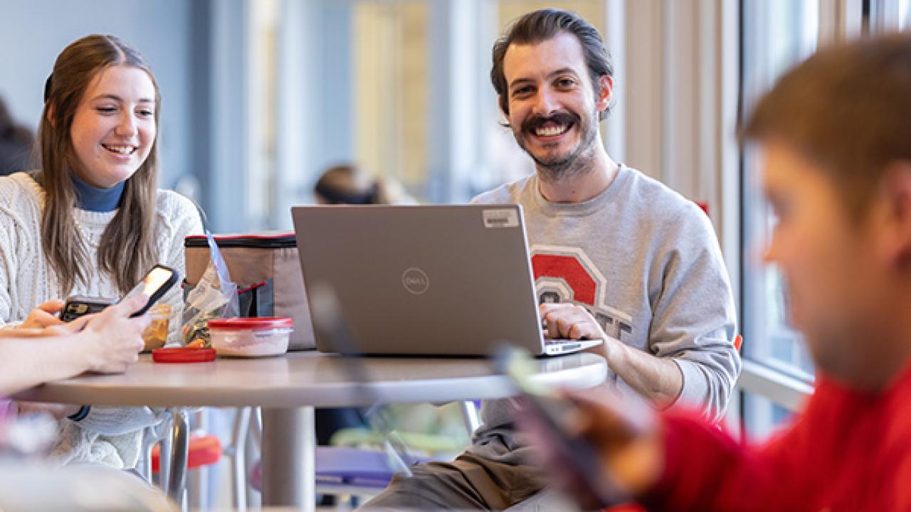 Students with a laptop smiling while eating food at a table